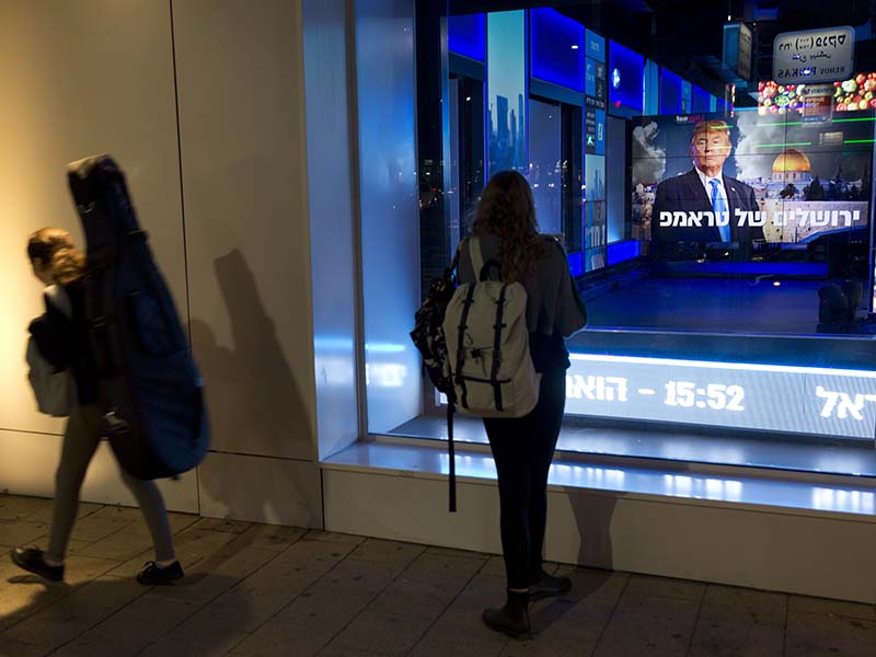 Israelis in Tel Aviv, Israel, walk next to a display with a photo of U.S. President Trump ahead of his speech Dec. 6, 2017. Defying dire, worldwide warnings, Trump on Wednesday broke with decades of U.S. and international policy by recognizing Jerusalem as Israel's capital. (AP Photo/Oded Balilty)