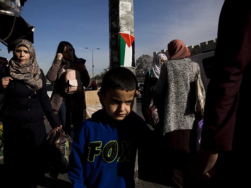 In this Sunday, Dec. 10, 2017 photo Palestinians walk by a national flag in east Jerusalem. (AP Photo/Oded Balilty - caption edited by RNS)