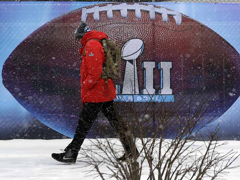 Snow falls as a man passes signage for the NFL Super Bowl 52 football game at U.S. Bank Stadium, Saturday, Feb. 3, 2018, in Minneapolis. The Philadelphia Eagles are scheduled to face the New England Patriots Sunday. (AP Photo/Eric Gay)