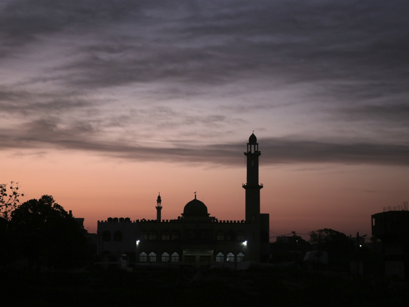 In this Wednesday, Jan. 3, 2018, photo, the sun rises over a mosque in Gaza City. In recent weeks, Gaza residents have been jolted awake in the dead of night by young men with loudspeakers calling them to early prayer. (AP Photo/Khalil Hamra)
