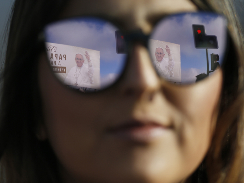 A banner welcoming Pope Francis is reflected in a woman's sunglasses as she waits for the pope's arrival at the Maquehue Air Base in Temuco, Chile, on Jan. 17, 2018. Francis heads to the heart of Chile's centuries-old conflict with indigenous peoples to celebrate Mass at the air base, which is on contested land that was also used as a detention and torture facility during the country's bloody military dictatorship. (AP Photo/Luis Hidalgo)