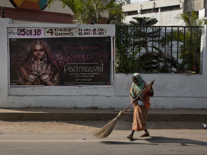 An Indian municipal worker sweeps a street in front of a 3D version of the Bollywood film 