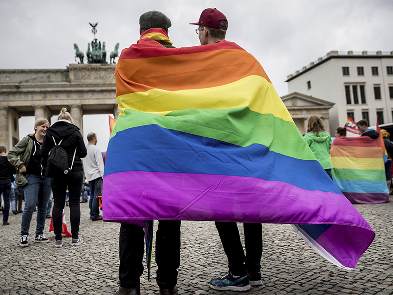 Men wrapped in a rainbow flag stand in front of the Brandenburg Gate in Berlin at an event to celebrate the legalization of same-sex marriage in Germany on June 30, 2017. (Michael Kappeler/dpa via AP)
