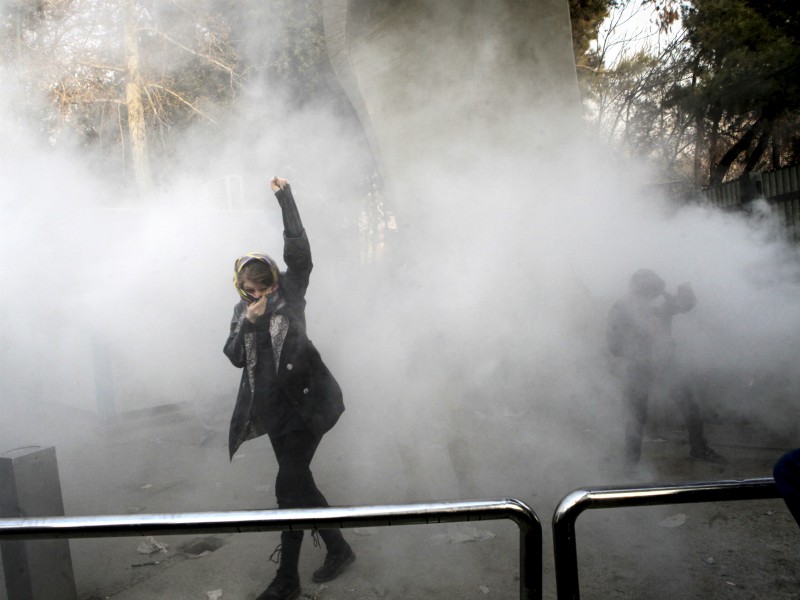 In this Dec. 30, 2017, file photo taken by an individual not employed by The Associated Press and obtained by AP outside Iran, a university student attends a protest inside Tehran University while a smoke grenade is thrown by anti-riot Iranian police, in Tehran, Iran. In 1979, massive crowds marched through the streets of Iran’s capital and other cities demanding change in the first major unrest to shake the rule of hard-line Muslim clerics. Now Iran’s Islamic Republic is seeing a new, equally startling wave of unrest. This time it appears to be fueled by anger over a still faltering economy, unemployment and corruption. (AP Photo, File) (Caption amended by RNS)