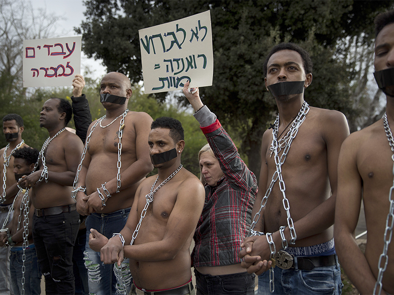 Eritrean migrants wear chains to mimic slaves at a demonstration Jan. 17, 2018, outside the Israeli Knesset in Jerusalem against the Israeli government’s policy to deport African refugees and asylum-seekers from Israel to Uganda and Rwanda. Hebrew signs read “no for deportation, Rwanda equal to death” and “slaves for sale.” (AP Photo/Oded Balilty)