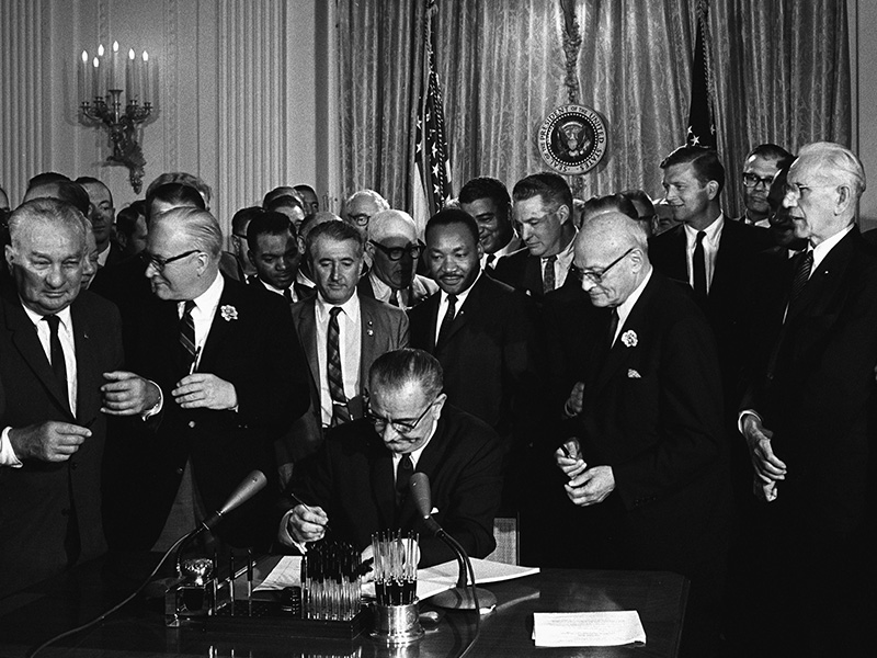 President Lyndon B. Johnson signs the 1964 Civil Rights Act as the Martin Luther King, Jr., and others, look on July 2, 1964. Photo by Cecil Stoughton, White House Press Office (WHPO) via Creative Commons