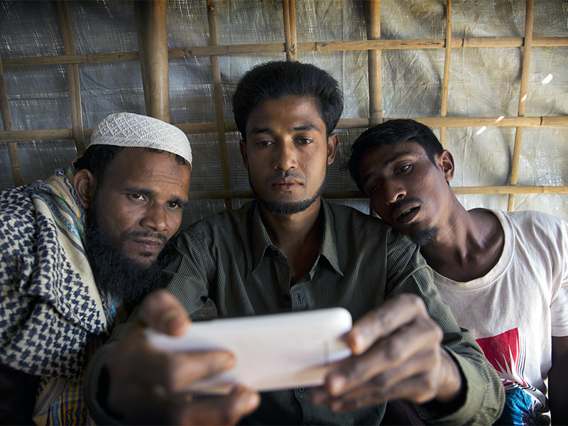 Rohingya Muslim refugee Mohammad Karim, 26, center, shows a mobile video of Gu Dar Pyin's massacre to other refugees in Kutupalong refugee camp, Bangladesh, on Jan. 14, 2018. On Sept. 9, a villager from Gu Dar Pyin captured three videos of mass graves that were time-stamped between 10:12 a.m. and 10:14 a.m., when he said soldiers chased him away. When he fled to Bangladesh, Karim removed the memory card from his phone, wrapped it in plastic and tied it to his thigh to hide it from Myanmar police. (AP Photo/Manish Swarup)