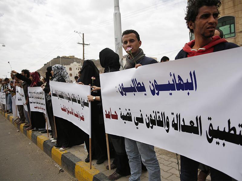 Members of the Baha'i faith protest outside a state security court during a hearing in the case of a fellow Baha'i man, Hamed bin Haydara, suspected of contacts with Israel and charged with seeking to establish a base for the community in Yemen, in Sanaa, Yemen, on April 3, 2016. Arabic writing on the poster at right, referring to the defendant, reads, 