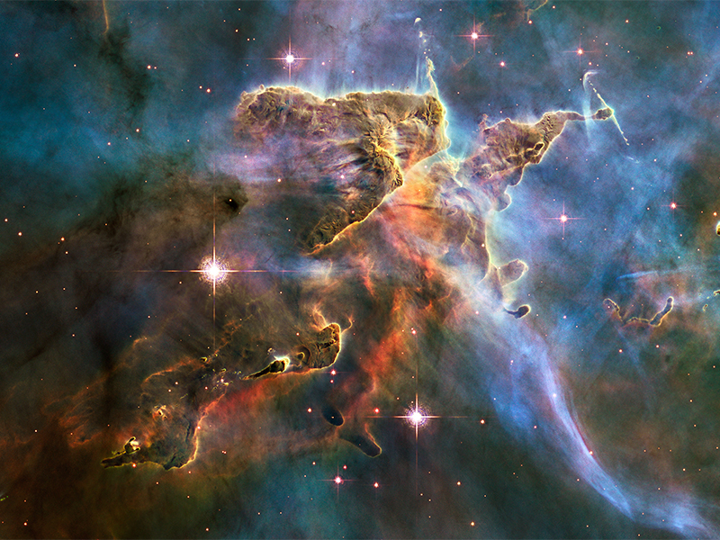 A Hubble photo is but a small portion of one of the largest seen star-birth regions in the galaxy, the Carina Nebula. Towers of cool hydrogen laced with dust rise from the wall of the nebula. Captured here are the top of a three-light-year-tall pillar of gas and the dust that is being eaten away by the brilliant light from nearby bright stars. Photo courtesy of NASA, ESA, and M. Livio and the Hubble 20th Anniversary Team (STScI)