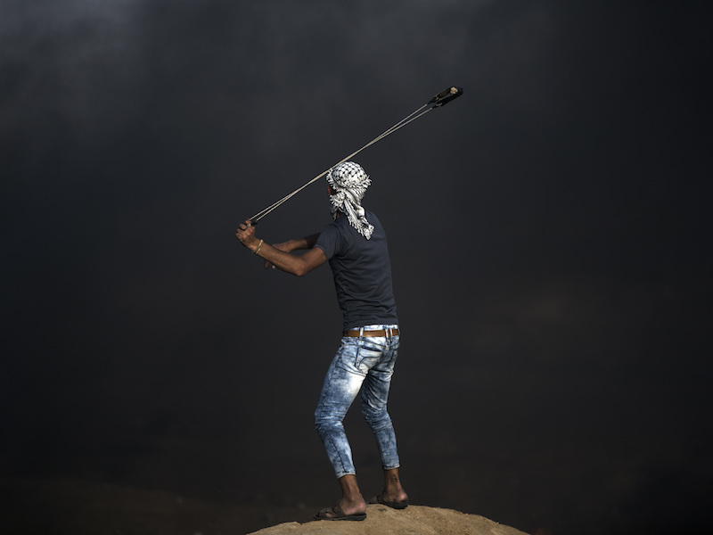 A Palestinian protester hurls stones at Israeli troops during a protest at the Gaza Strip's border with Israel on May 18, 2018. (AP Photo/Khalil Hamra)
