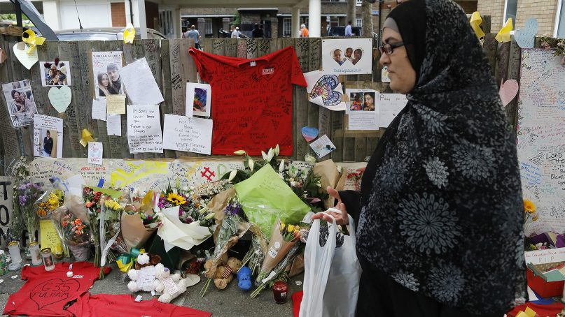 A womna passes T-shirts left by firefighters with messages and flowers in tribute to the missing people, near the Grenfell Tower apartment building in London, on June 23, 2017. British officials have ordered an immediate examination Friday, into a fridge-freezer that is deemed to have started the fire in the 24-storey high-rise apartment building early morning of June 14th, and the outside cladding of the building which is thought to have helped spread the fire, according to police, leaving dozens dead. (AP Photo/Frank Augstein)