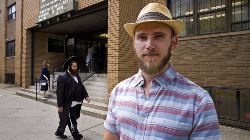 In this July 18, 2018, photo, Pesach Eisen poses in front of a yeshiva he attended as a child in the Borough Park neighborhood in Brooklyn, N.Y. Eisen, now 32, left his Orthodox community in his late teens. Complaints that schools like Eisen's run by New York's strictly observant Hasidic Jews barely teach English, math, science or social studies have fueled a movement to demand stricter oversight by state and local educational authorities.  (AP Photo/Mark Lennihan)