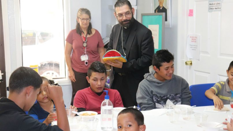 Bishop Daniel Flores of Brownsville meets with children and families at the Humanitarian Respite Center in McAllen, Texas, during a recent delegation trip. Photo courtesy of Ashley Feasley