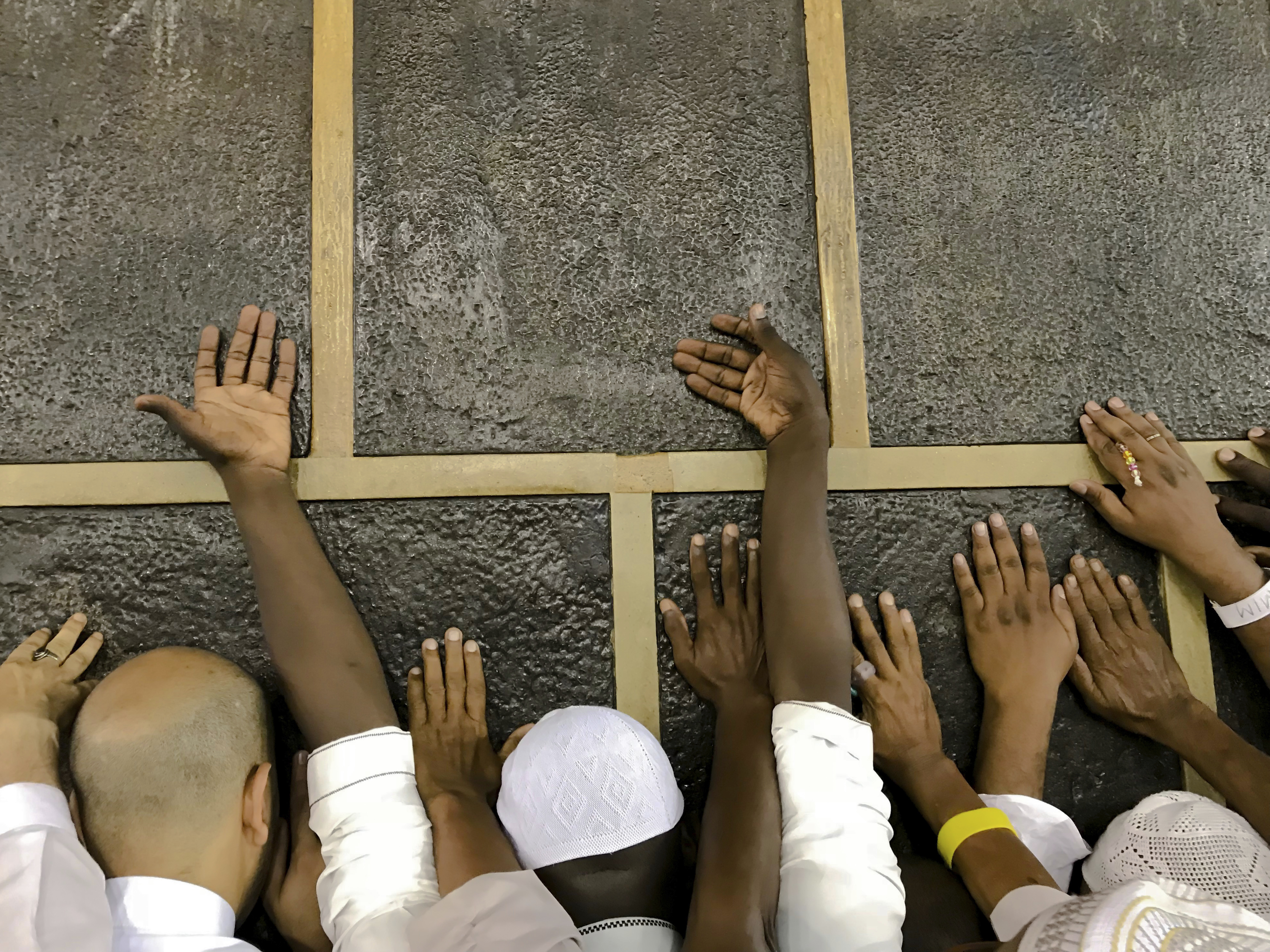 Muslim pilgrims touch the Kaaba stone, the cubic building at the Grand Mosque, as they pray ahead of the annual Hajj pilgrimage in the Muslim holy city of Mecca, Saudi Arabia, Friday, Aug. 17, 2018. The annual Islamic pilgrimage draws millions of visitors each year, making it the largest yearly gathering of people in the world. (AP Photo/Dar Yasin)