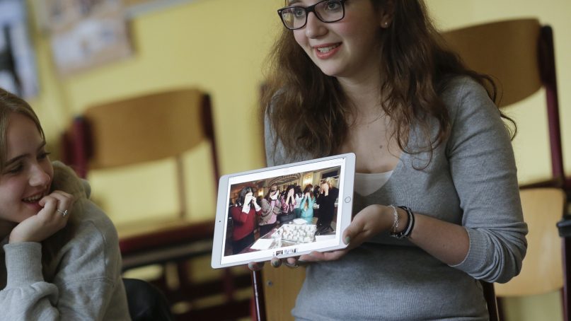 In this June 25, 2018, photo, Jewish teenager Sophie Steiert, right, shows a picture of Jewish daily life on a tablet computer as Laura Schulmann looks on during a lesson as part of a project of religions at the Bohnstedt Gymnasium high school in Luckau, Germany. With the number of Holocaust survivors dwindling and schoolchildren now at least three generations removed from the Nazi genocide, teenagers have been recruited as the next ambassadors for the Jewish community in Germany. (AP Photo/Markus Schreiber)