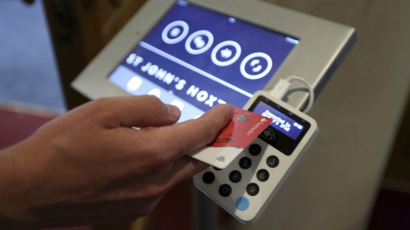 In this photo taken on Aug. 2, 2018, Aaron Rodewald, an operations and finance manager at St. John's Church, demonstrates a device that allows churchgoers to donate money using contactless payments, in Hoxton, London. Thousands of Christian churches across the world are now using portable card readers or apps to take donations as people increasingly stop carrying cash on them. The Church of England says 16,000 religious sites now have access to portable card readers. In the U.S., hundreds of churches have installed kiosks where the faithful can swipe a card to donate. (AP Photo/Robert Stevens)
