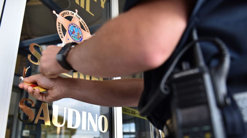 A Bergen County, N.J., sheriff's officer uses a razor blade to peel off the name of Michael Saudino, who resigned on Friday as sheriff of Bergen County, in gold letters from the glass entrance of the Bergen County Jail in Hackensack, on Sept. 24, 2018. Photo by Tariq Zehawi/NorthJersey.com via USAToday
