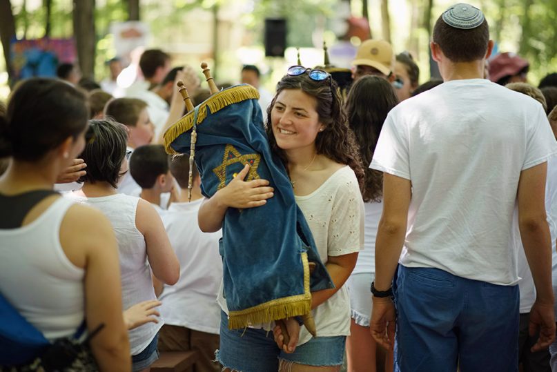 A female carries the Torah during a service at URJ Camp Harlam in Kunkletown, Penn., in the summer of 2016. Photo copyright Foundation for Jewish Camp