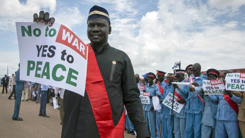 South Sudanese demonstrators hold signs requesting peace as they await the arrival of South Sudan's president, Salva Kiir, at the airport in Juba, South Sudan, on June 22, 2018. (AP Photo/Bullen Chol)
