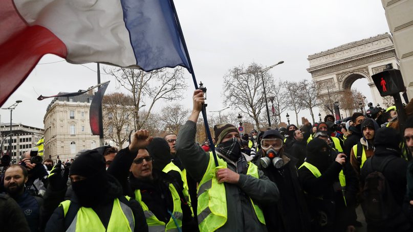 Demonstrators wearing yellow vests march near the Arc de Triomphe, right, holding the French tricolor in Paris, on Dec. 8, 2018.  (AP Photo/Thibault Camus)