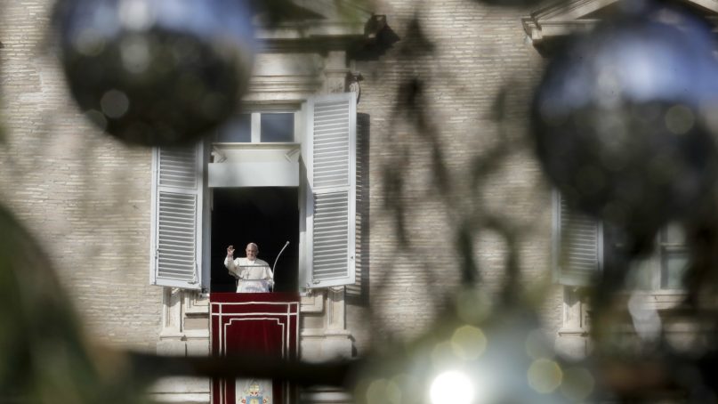 Pope Francis, framed between the branches of a Christmas tree, greets the faithful he recites the Angelus noon prayer from the window of his studio overlooking St.Peter's Square, at the Vatican, Sunday, Dec. 23, 2018. (AP Photo/Andrew Medichini)
