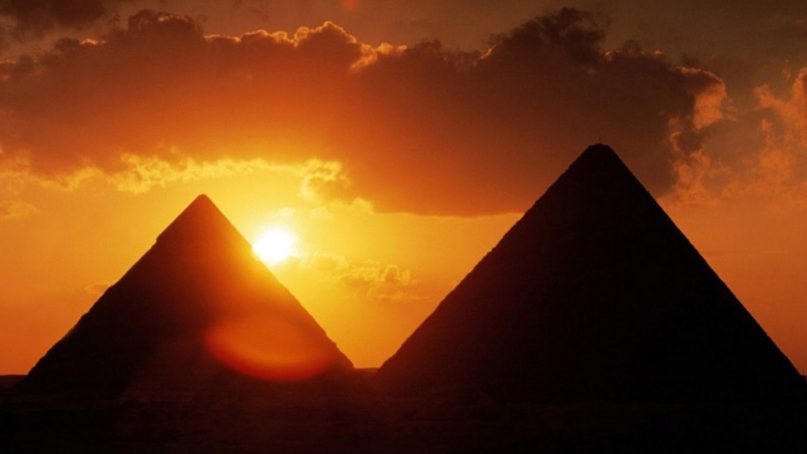 The sun sets between two pyramids in Egypt. Photo courtesy of Creative Commons