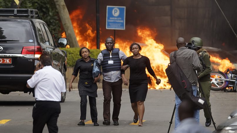 Security forces help civilians flee the scene of a terrorist attack, as cars burn in the background, at a hotel complex in Nairobi, Kenya, on Jan. 15, 2019. Extremists launched an attack on a luxury hotel in Kenya's capital, sending people fleeing in panic as explosions and heavy gunfire reverberated through the neighborhood. Al-Shabab, the Somalia-based extremist group, has claimed responsibility. (AP Photo/Ben Curtis)