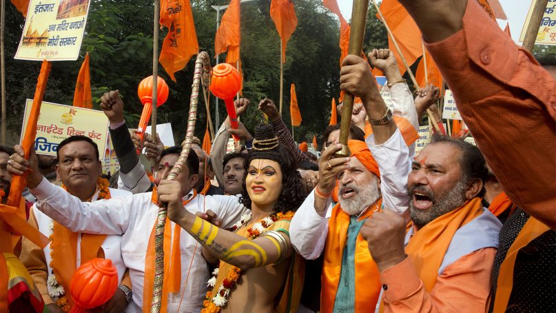A man stands dressed as the Hindu god Ram, center, in New Delhi on Dec. 6, 2018, as activists of right-wing Hindu groups shout slogans demanding that a temple of Ram be built at Ayodhya in northern India. Hard-line Hindus are demanding that the temple be built on the site where, in 1992, Hindu extremists attacked and demolished the 16th-century Babri mosque, sparking deadly Hindu-Muslim violence.  (AP Photo/Manish Swarup)