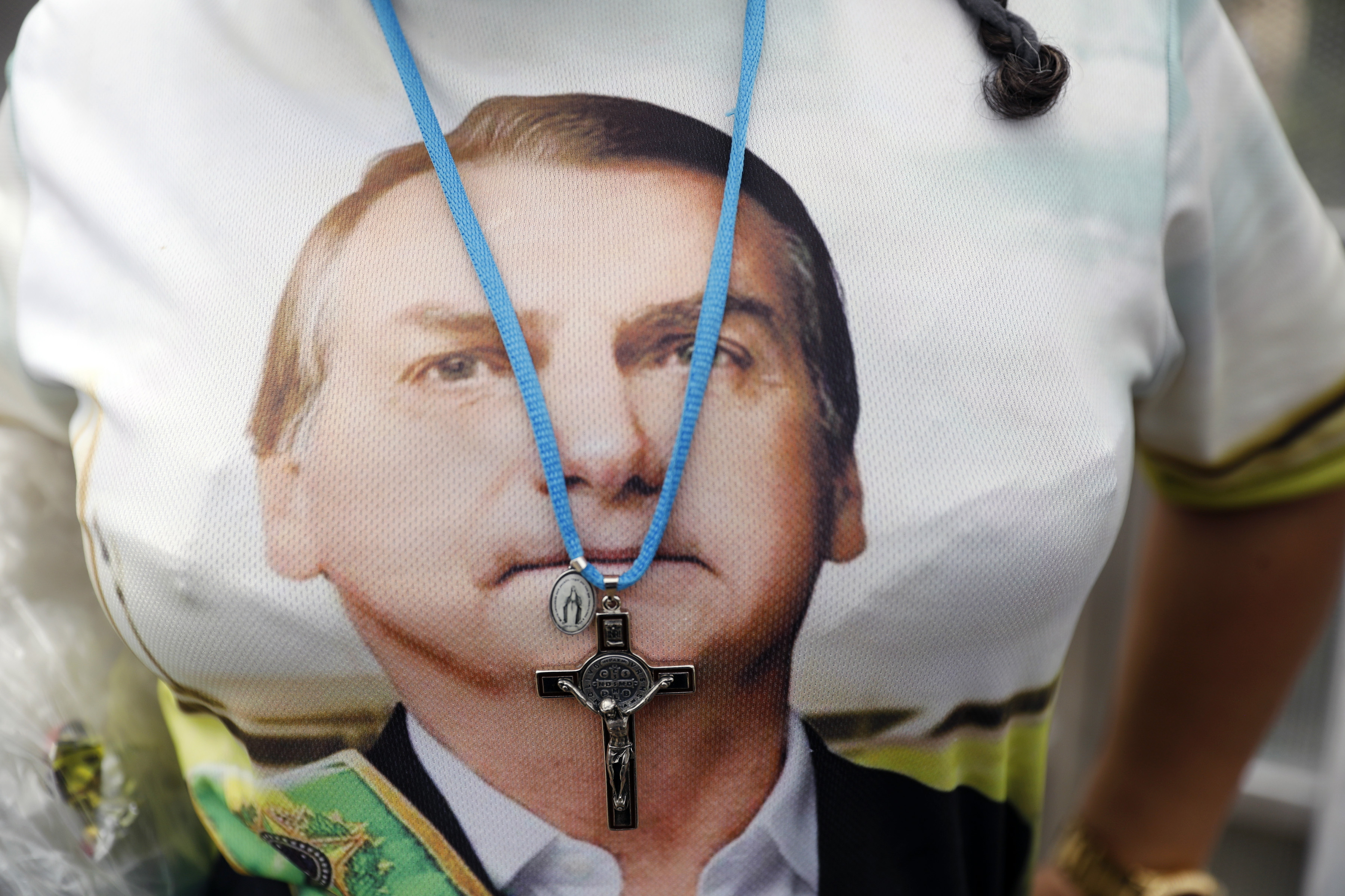 A supporter of Brazil's President Jair Bolsonaro wears a crucifix necklace over a shirt with Bolsonaro’s likeness prior to Bolsonaro's inauguration, in Brasilia, Brazil, on Jan. 1, 2019. (AP Photo/Silvia Izquierdo)
