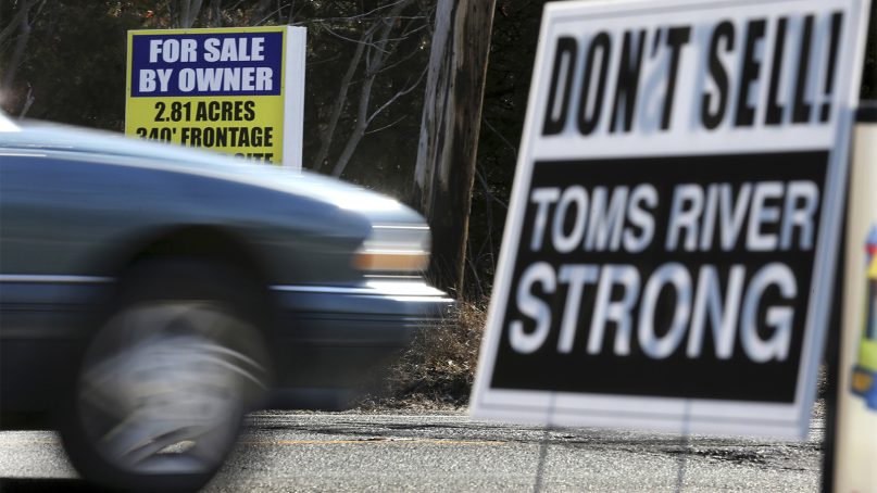 A for sale sign is seen across the street from a don't sell, Toms River strong sign on Feb. 22, 2016, in Toms River, N.J.  A housing crunch in the New Jersey shore town that’s home to one of the nation’s largest Hasidic populations has neighboring towns changing their own laws. Real estate agents and investors in the Lakewood area have been soliciting residents in several nearby neighborhoods, looking to find homes that fit the needs of the growing Jewish community. (AP Photo/Mel Evans)