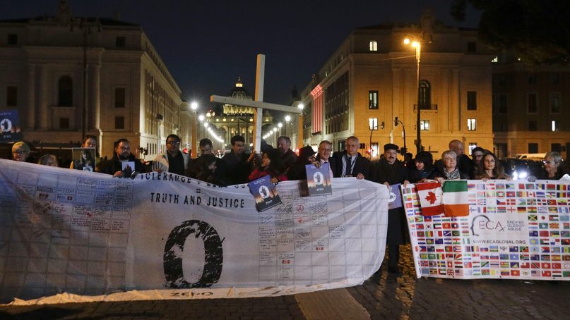 Survivors of clerical sex abuse hold a cross as they gather in front of Via della Conciliazione, the road leading to St. Peter’s Square, visible in background, during a twilight vigil prayer of the victims of sex abuse, in Rome, on Feb. 21, 2019. (AP Photo/Gregorio Borgia)
