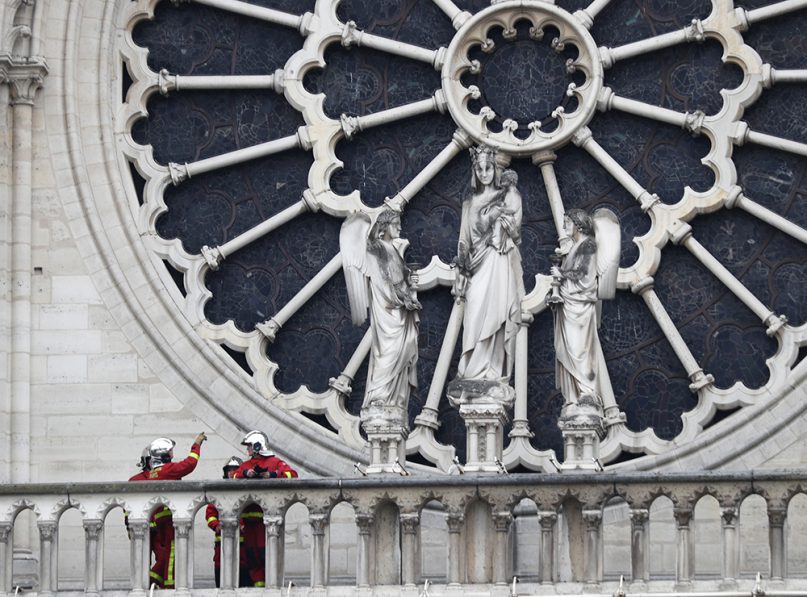 Parisian firefighters talk near the rose window of Notre Dame Cathedral on April 16, 2019, in Paris. Experts assessed the blackened shell of Paris' iconic Notre Dame Tuesday morning to establish next steps to save what remains after a devastating fire destroyed much of the cathedral that had survived almost 900 years of history. (AP Photo/Thibault Camus)