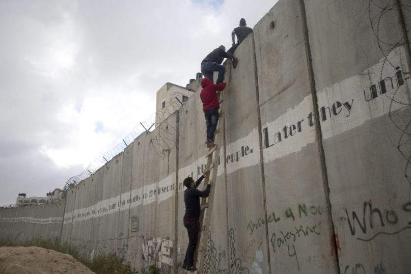 Palestinians climb the Israeli separation barrier on their way to attend the first Friday prayers in Jerusalem's al-Aqsa mosque, during the Muslim holy month of Ramadan, in the village of al Ram, on May 10, 2019. (AP Photo/Majdi Mohammed)