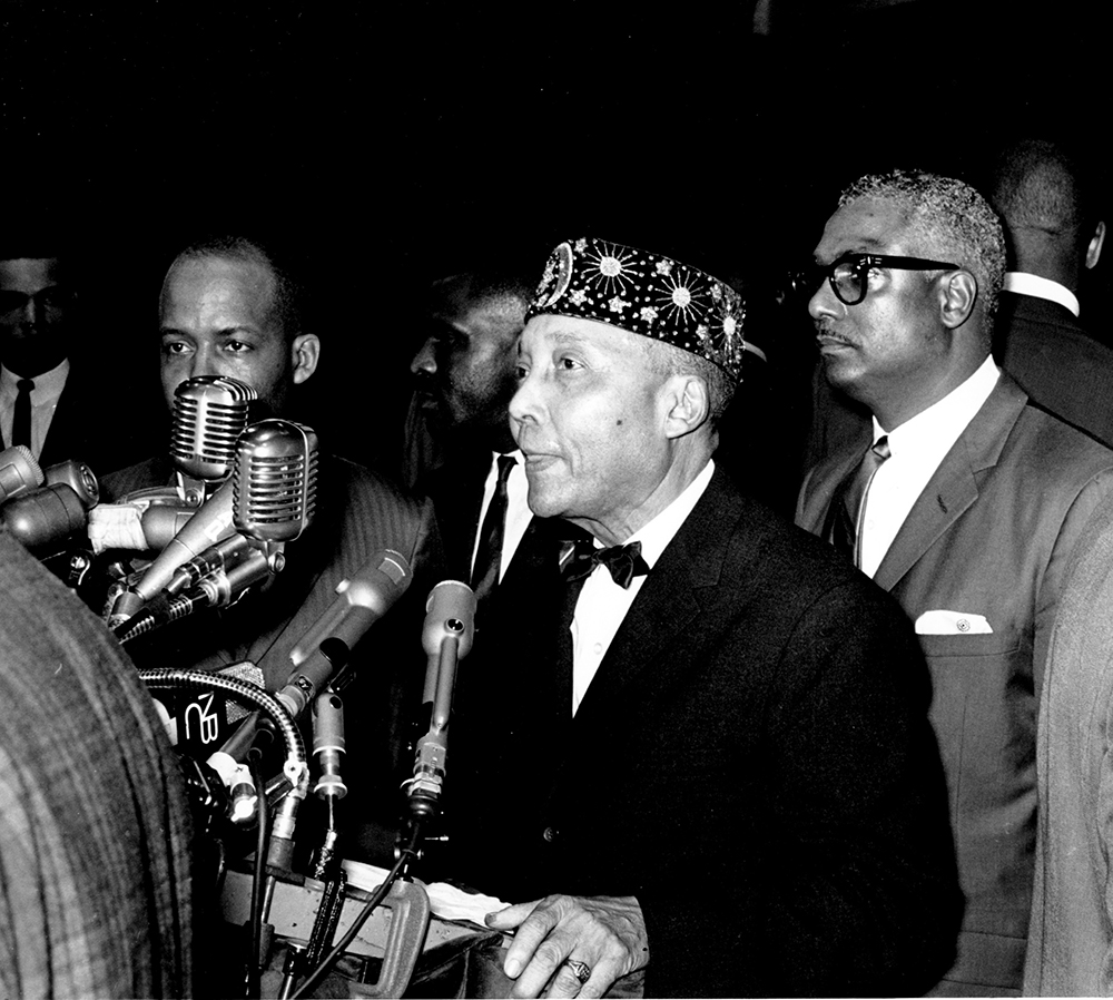 Elijah Muhammad, leader of the American black Muslim organization the Nation of Islam, addresses the concluding session of the annual convention at Chicago Coliseum, Ill., on Feb. 28, 1966. He is flanked by bodyguards. (AP Photo)