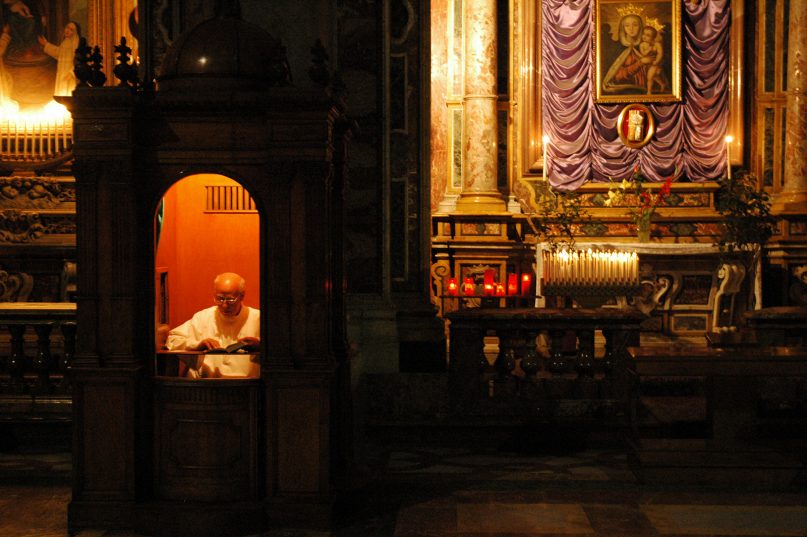 A priest reads inside a confessional.  Photo by Emilio Labrador/Creative Commons