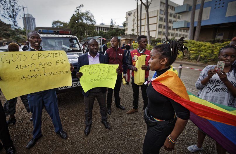 An activist supporting the LGBT community, wearing a rainbow flag, walks past a gathering of Christians opposed to the decriminalization of homosexuality, after a ruling by the High Court in Nairobi, Kenya, Friday, May 24, 2019. Kenya's High Court on Friday upheld sections of the penal code that criminalize same-sex relations, a disappointment for gay rights activists across Africa where dozens of countries have similar laws. (AP Photo/Ben Curtis)