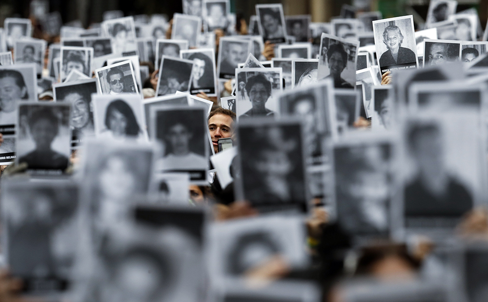 A man stands amid pictures of victims of the bombing of the AMIA Jewish center that killed 85 people, on the 25th anniversary of the attack, in Buenos Aires, Argentina, on July 18, 2019. (AP Photo/Natacha Pisarenko)