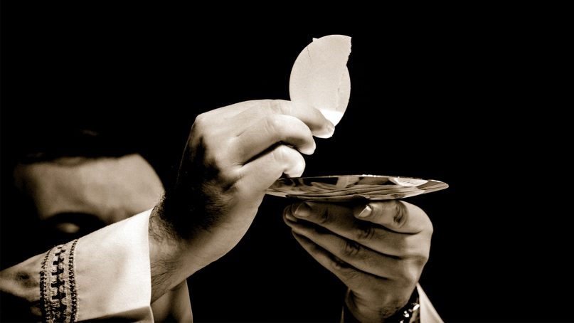 A priest holds up the Eucharist. Photo by Robert Cheaib/Creative Commons