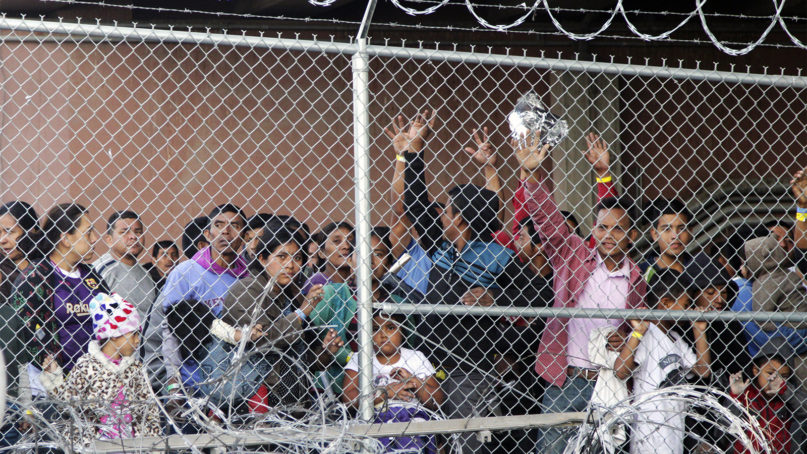 Central American migrants wait for food in El Paso, Texas, on March 27, 2019, in a pen erected by U.S. Customs and Border Protection to process a surge of migrant families and unaccompanied minors. Earlier, Customs and Border Protection Commissioner Kevin McAleenan, center, announced the the Trump administration will temporarily reassign several hundred border inspectors, during a news conference at the border in El Paso. (AP Photo/Cedar Attanasio)