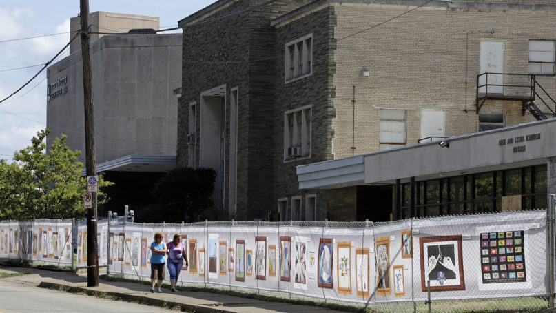 Passers by look at art that is displayed on a fence surrounding the Tree of Life synagogue in Pittsburgh on Tuesday, Sept. 17, 2019. The first anniversary of the shooting at the synagogue, that killed 11 worshippers, is Oct. 27, 2019. (AP Photo/Gene J. Puskar)