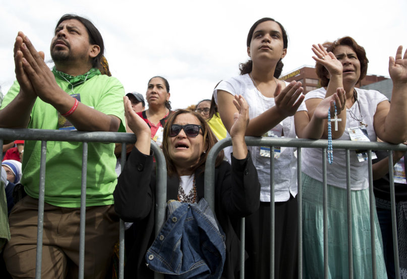 Milagros Orengo, second from left, her daughter Emily Orengo and Maria Santos, right, all from Egg Harbor, N.J., pray behind a barricade at Independence Mall in Philadelphia, as a Mass with Pope Francis at the Cathedral Basilica of Sts. Peter and Paul is projected on a large screen, Saturday, Sept. 26, 2015. (AP Photo/Carolyn Kaster)