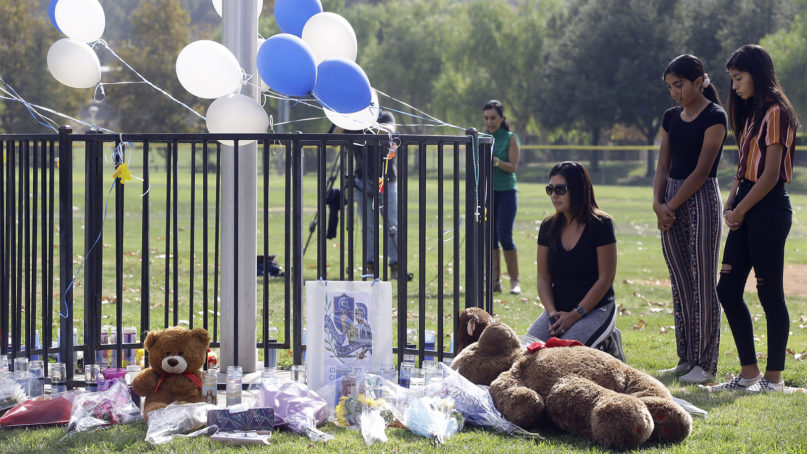 Parent Mirna Herrera kneels with her daughters Liliana, 15, and Alexandra, 16, at the Central Park memorial for the Saugus High School victims in Santa Clarita, Calif., Friday, Nov. 15, 2019. Investigators said Friday they have yet to find a diary, manifesto or note that would explain why a boy killed two students outside his Southern California high school on his 16th birthday. (AP Photo/Damian Dovarganes)