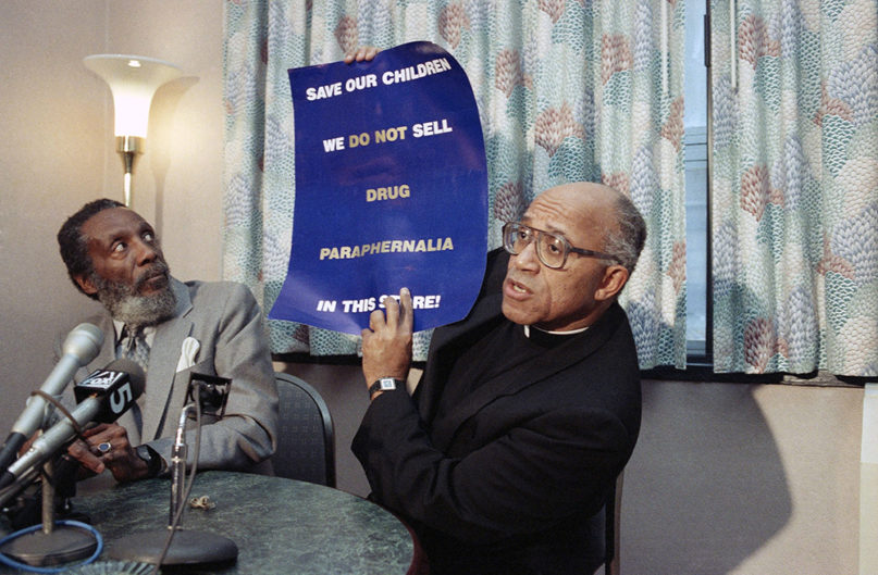 In a Jan. 22, 1990 file photo, Dick Gregory, left, looks at a sign held by Rev. George Clements, of Chicago, during a press conference in New York, to introduce their campaign to combat drug use in Times Square. The Rev. George Clements, the Chicago priest whose civil rights and social justice activism prompted the making of a movie about his life died Monday, Nov. 25, 2019 in a Hammond, Indiana hospital according to the Archdiocese of Chicago. He was 87.  (AP Photo/Frankie Ziths)