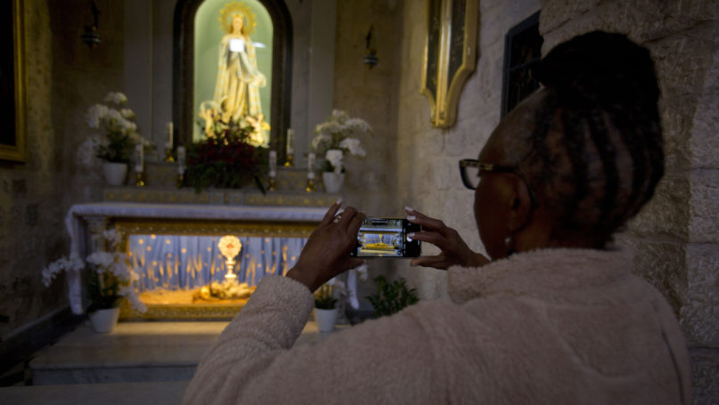 In this Dec. 5, 2019, photo, a Christian visitor takes a picture of a wooden relic believed to be from Jesus' manger inside the Church of the Nativity, traditionally believed by Christians to be the birthplace of Jesus Christ, in the West Bank city of Bethlehem. As visitors descend on Bethlehem this Christmas, they have the option of staying in restored centuries-old guesthouses, taking food tours of local markets and perusing the dystopian art in and around a hotel designed by the British graffiti artist Banksy. (AP Photo/Majdi Mohammed)