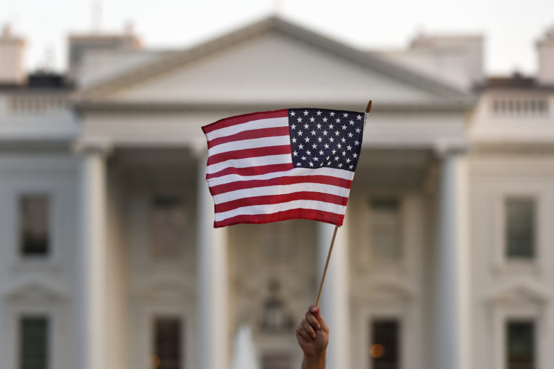 FILE - In this Sept. 2017 file photo, a flag is waved outside the White House, in Washington.  The Trump administration announced Friday that it was curbing legal immigration from six additional countries that officials said did not meet security screening standards, as part of an election-year push to further restrict immigration. Officials said immigrants from Kyrgyzstan, Myanmar, Eritrea, Nigeria, Sudan and Tanzania will face new restrictions in obtaining certain visas to come to the United States. But it is not a total travel ban, unlike President Donald Trump’s earlier effort that generated outrage around the world for unfairly targeting Muslims. (AP Photo/Carolyn Kaster)