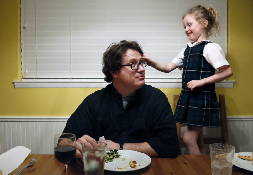 In this Feb. 7, 2020, photo, converted Catholic Priest Joshua Whitfield of north Dallas, left, looks up at his daughter Zoe-Catherine, 5, who stands on a kitchen chair pressing a pink butterfly clip into his hair during dinner in north Dallas. (AP Photo/Jessie Wardarski)