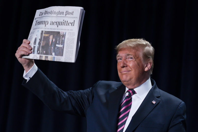 President Donald Trump holds up a newspaper with the headline that reads 