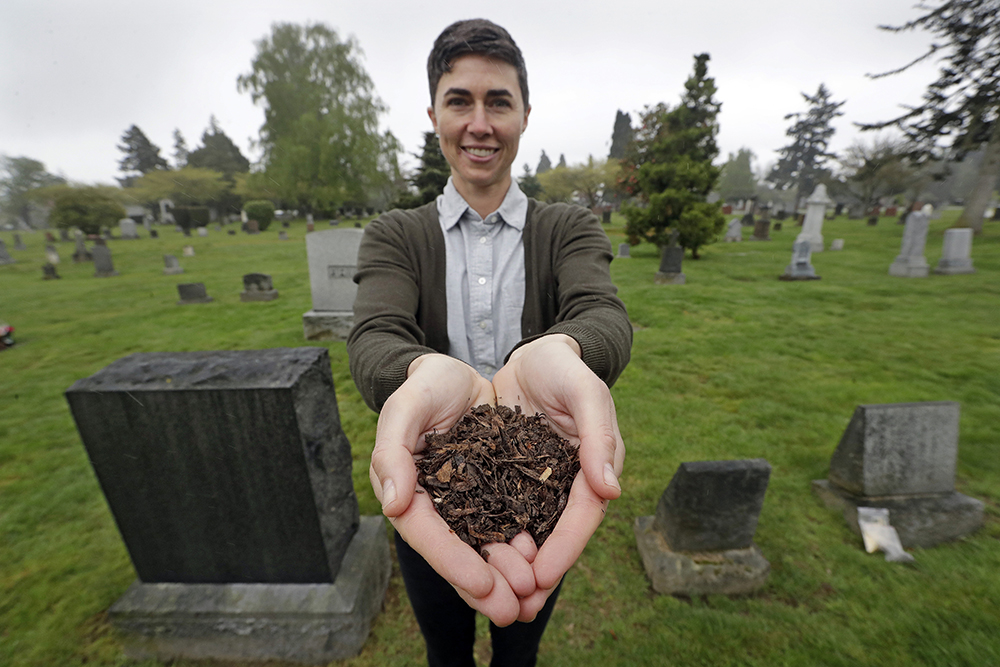 In this April 19, 2019, file photo, Katrina Spade, the founder and CEO of Recompose, a company that hopes to use composting as an alternative to burying or cremating human remains, poses for a photo in a cemetery in Seattle, as she displays a sample of compost material left from the decomposition of a cow using a combination of wood chips, alfalfa and straw. On Tuesday, May 21, 2019, Washington Gov. Jay Inslee signed a bill into law that allows licensed facilities to offer "natural organic reduction," which turns a body, mixed with substances such as wood chips and straw, into soil. Th law makes Washington the first state in the U.S. to approve composting as an alternative to burying or cremating human remains. (AP Photo/Elaine Thompson, File)