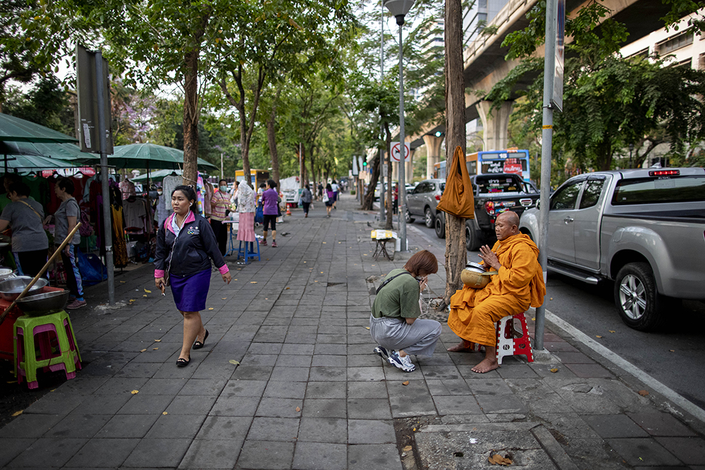 A devotee with a protective mask receives a blessing after offering alms to a Buddhist monk on a sidewalk in Bangkok, Thailand, Tuesday, March 17, 2020. (AP Photo/Gemunu Amarasinghe)