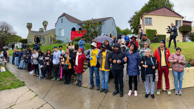 Activists in support of people occupying a vacant home, center, link arms in a barricade as police arrive, Saturday, March 14, 2020, in Los Angeles. The occupied home is owned by the California Department of Transportation. Photo courtesy of Reclaiming Our Homes